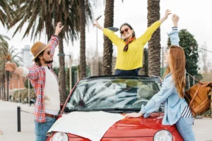 Turistas celebram viagem em volta de um carro vermelho, prontos para explorar como dirigir em Orlando com um veículo alugado.