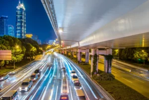 A imagem mostra uma rua com vários carros, representando as regras de trânsito dos EUA. É possível ver um prédio ao fundo.