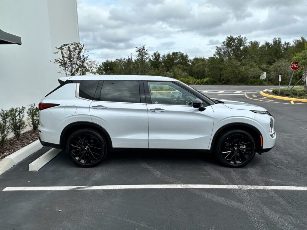 SUV branco moderno da Move estacionado em área pavimentada junto a prédio industrial cinza, com árvores e céu parcialmente nublado ao fundo.